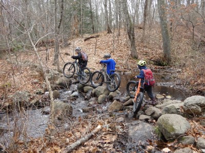 the boys walking their bikes on rocks across a stream