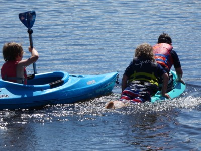 Zion and a friend half-on a tiny kayak, Lijah paddling a regular one