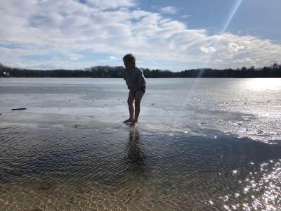 Zion, in shorts and bare feet, standing on pond ice in front of open water