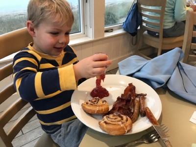 Zion pouring ketchup onto his plate of sausages, bacon, and danishes